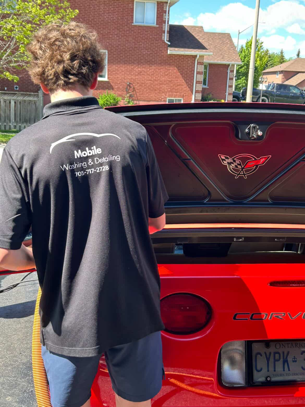 Cole detailing a red Corvette in his Barrie Mobile Washing & Detailing polo